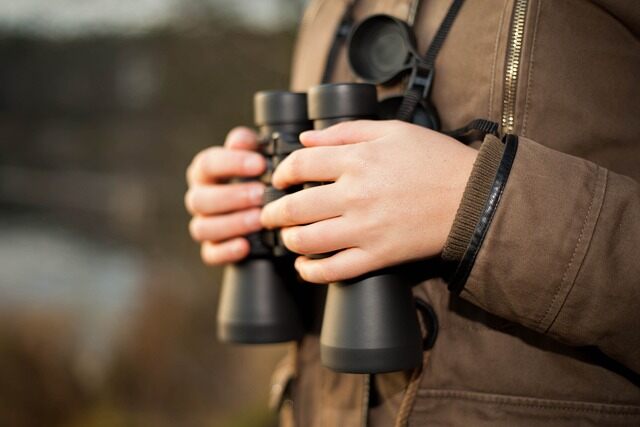 A person holding a pair of binoculars while out birdwatching.