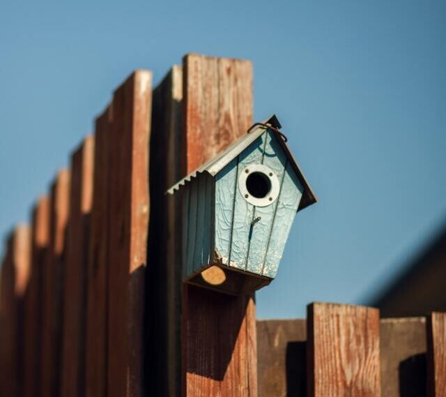 A blue birdhouse perched on a wooden fence.