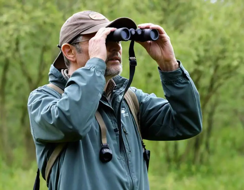 A birdwatcher watching a bird with his binoculars.