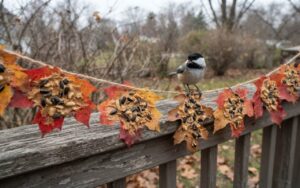 A raw, unedited photo of an autumn leaf garland coated in peanut butter and birdseed hanging on a porch rail as a chickadee feeds on an overcast morning.